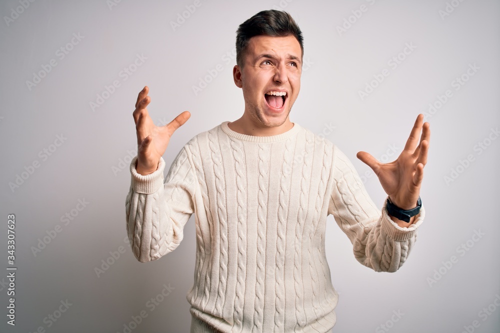 Young handsome caucasian man wearing casual winter sweater over white isolated background crazy and mad shouting and yelling with aggressive expression and arms raised. Frustration concept. Young handsome caucasian man wearing casual winter sweater over white isolated background crazy and mad shouting and yelling with aggressive expression and arms raised. Frustration concept.