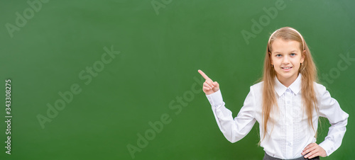 Happy young  girl points away on empty green chalkboard. Empty space for text