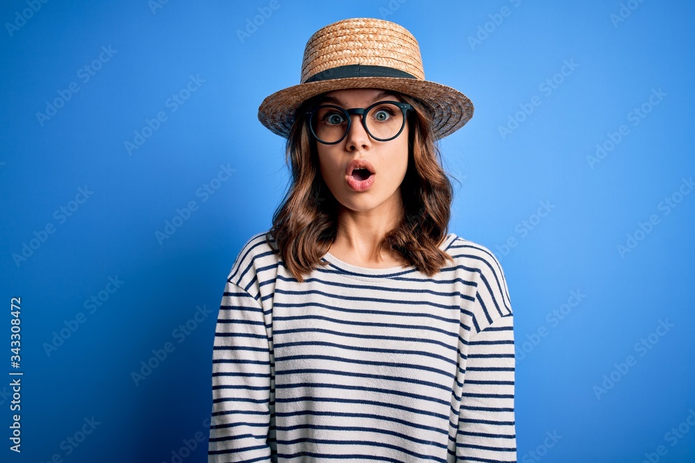 Young beautiful blonde girl wearing glasses and hat over blue isolated background scared in shock with a surprise face, afraid and excited with fear expression Young beautiful blonde girl wearing glasses and hat over blue isolated background scared in shock with a surprise face, afraid and excited with fear expression