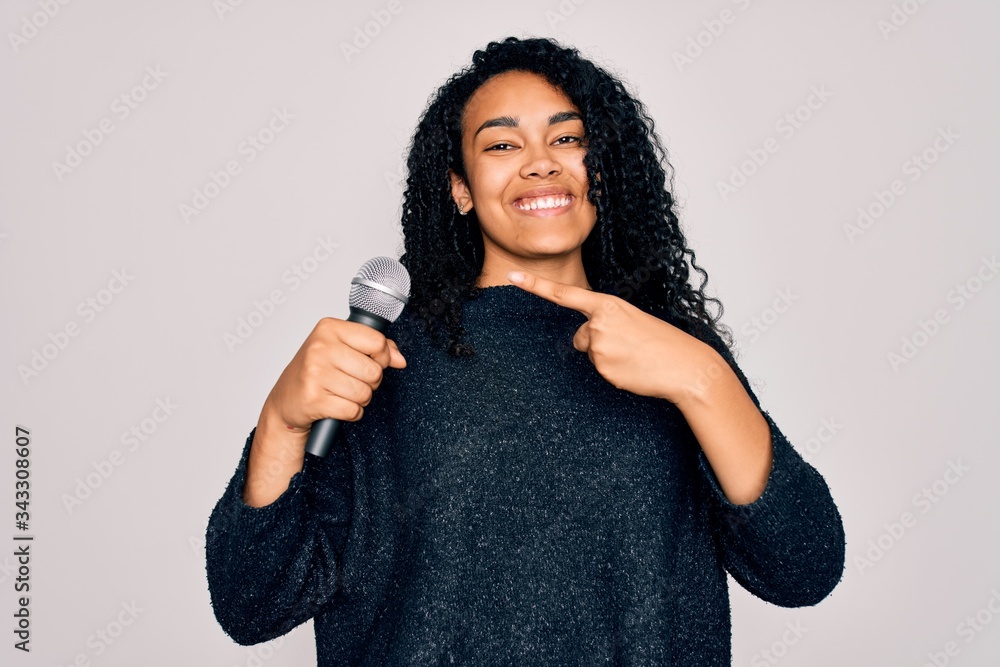 Young african american curly singer woman singing using microphone over white background very happy pointing with hand and finger Young african american curly singer woman singing using microphone over white background very happy pointing with hand and finger