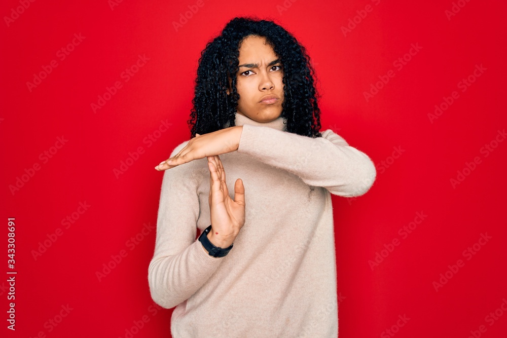 Fototapeta premium Young african american curly woman wearing casual turtleneck sweater over red background Doing time out gesture with hands, frustrated and serious face