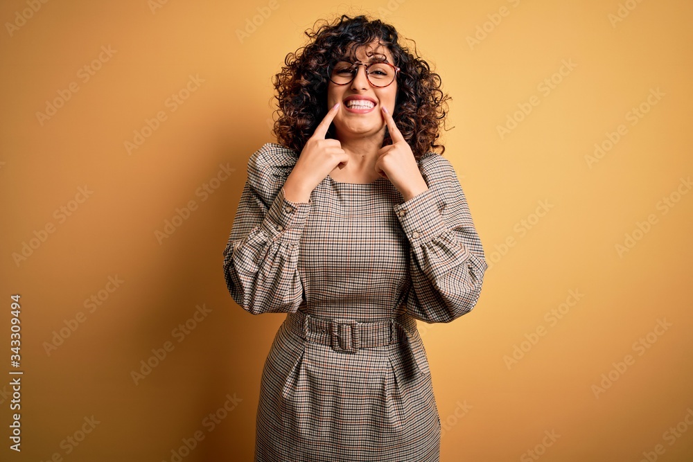 Beautiful arab business woman wearing dress and glasses standing over yellow background Smiling with open mouth, fingers pointing and forcing cheerful smile Beautiful arab business woman wearing dress and glasses standing over yellow background Smiling with open mouth, fingers pointing and forcing cheerful smile