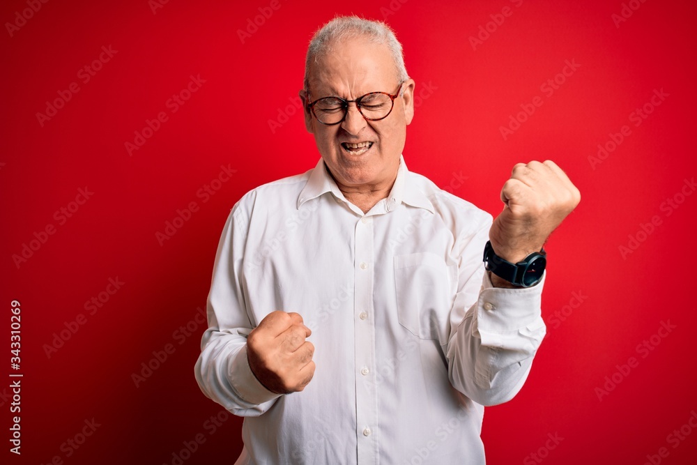 Middle age handsome hoary man wearing casual shirt and glasses over red background celebrating surprised and amazed for success with arms raised and eyes closed. Winner concept. Middle age handsome hoary man wearing casual shirt and glasses over red background celebrating surprised and amazed for success with arms raised and eyes closed. Winner concept.