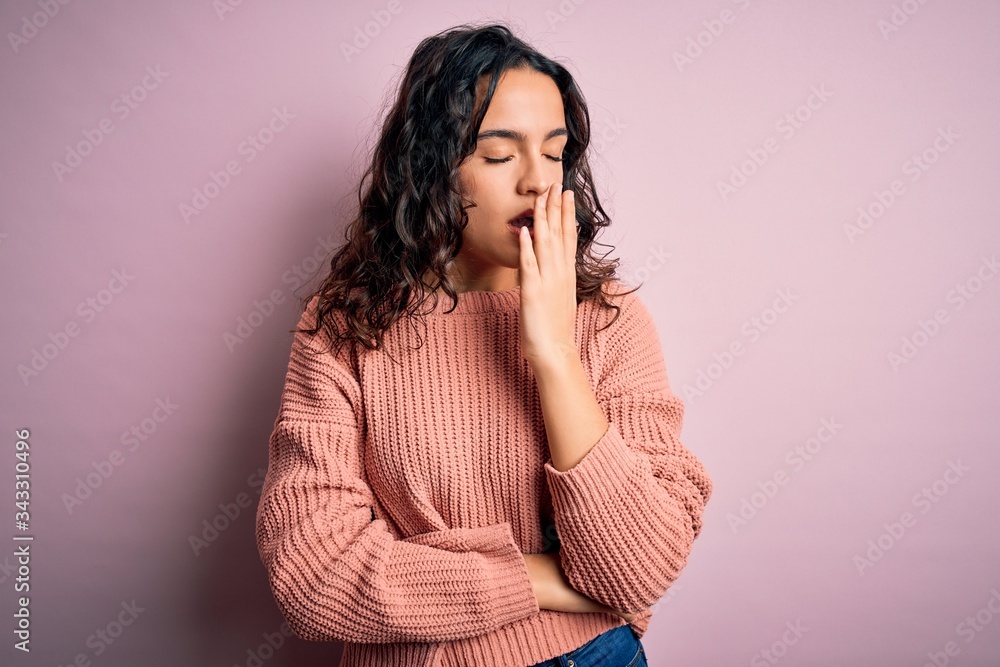 Young beautiful woman with curly hair wearing casual sweater over isolated pink background bored yawning tired covering mouth with hand. Restless and sleepiness. Young beautiful woman with curly hair wearing casual sweater over isolated pink background bored yawning tired covering mouth with hand. Restless and sleepiness.