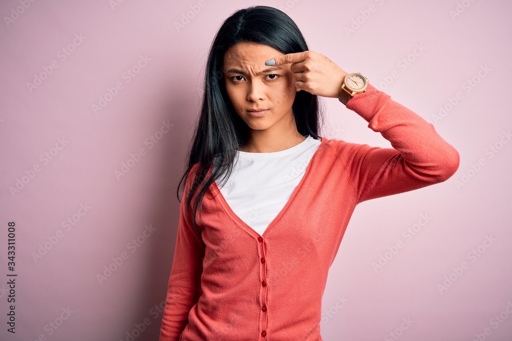 Young beautiful chinese woman wearing casual sweater over isolated pink background pointing unhappy to pimple on forehead, ugly infection of blackhead. Acne and skin problem Young beautiful chinese woman wearing casual sweater over isolated pink background pointing unhappy to pimple on forehead, ugly infection of blackhead. Acne and skin problem