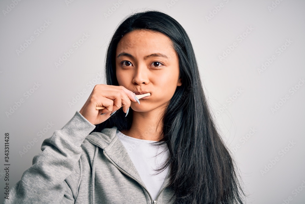 Young beautiful woman standing whasing tooth using toothbrush over isolated white background Young beautiful woman standing whasing tooth using toothbrush over isolated white background