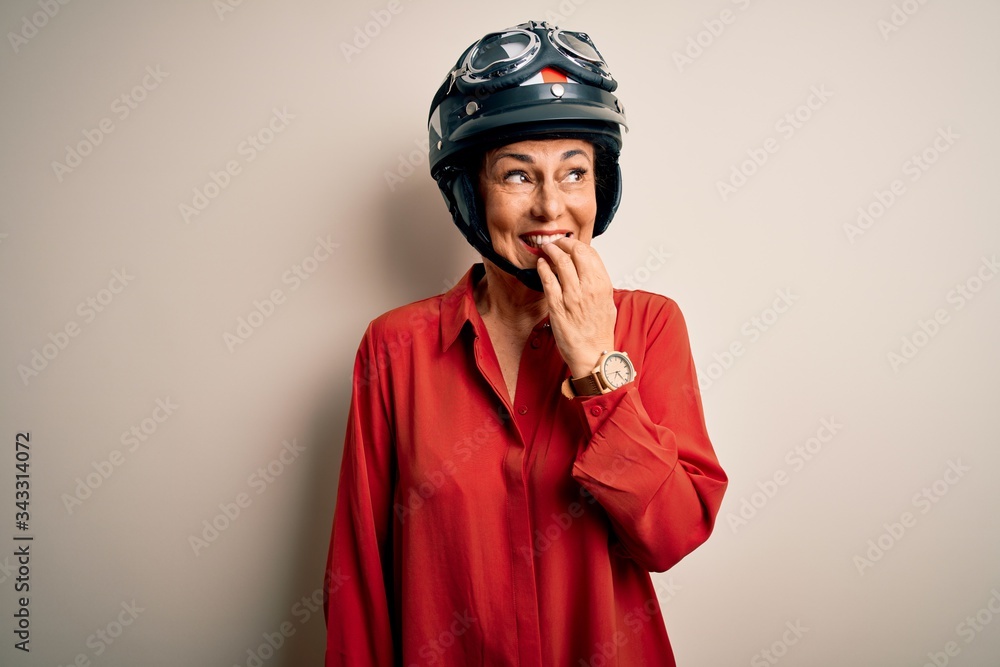 Middle age motorcyclist woman wearing motorcycle helmet over isolated white background looking stressed and nervous with hands on mouth biting nails. Anxiety problem. Middle age motorcyclist woman wearing motorcycle helmet over isolated white background looking stressed and nervous with hands on mouth biting nails. Anxiety problem.