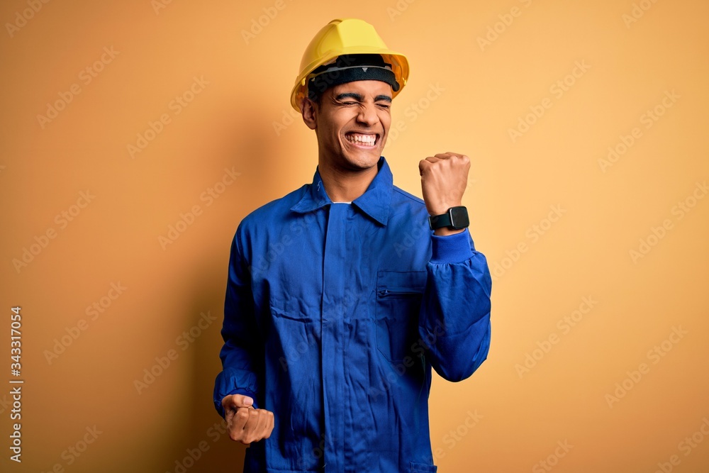 Young handsome african american worker man wearing blue uniform and security helmet celebrating surprised and amazed for success with arms raised and eyes closed. Winner concept.