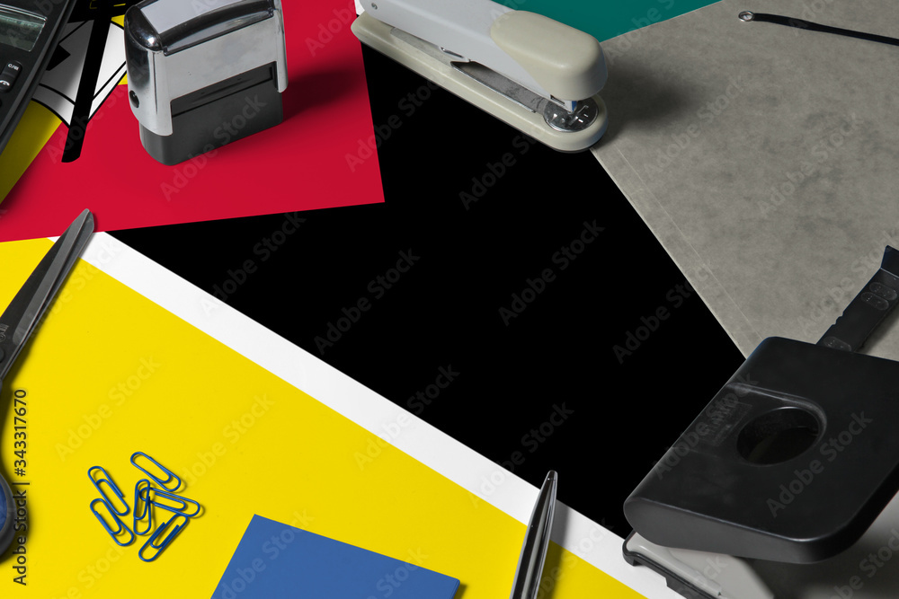 Obraz premium Mozambique flag with office clerk workplace background. National stationary concept with office tools.