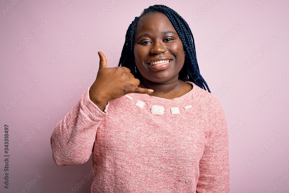 African american plus size woman with braids wearing casual sweater over pink background smiling doing phone gesture with hand and fingers like talking on the telephone. Communicating concepts. African american plus size woman with braids wearing casual sweater over pink background smiling doing phone gesture with hand and fingers like talking on the telephone. Communicating concepts.