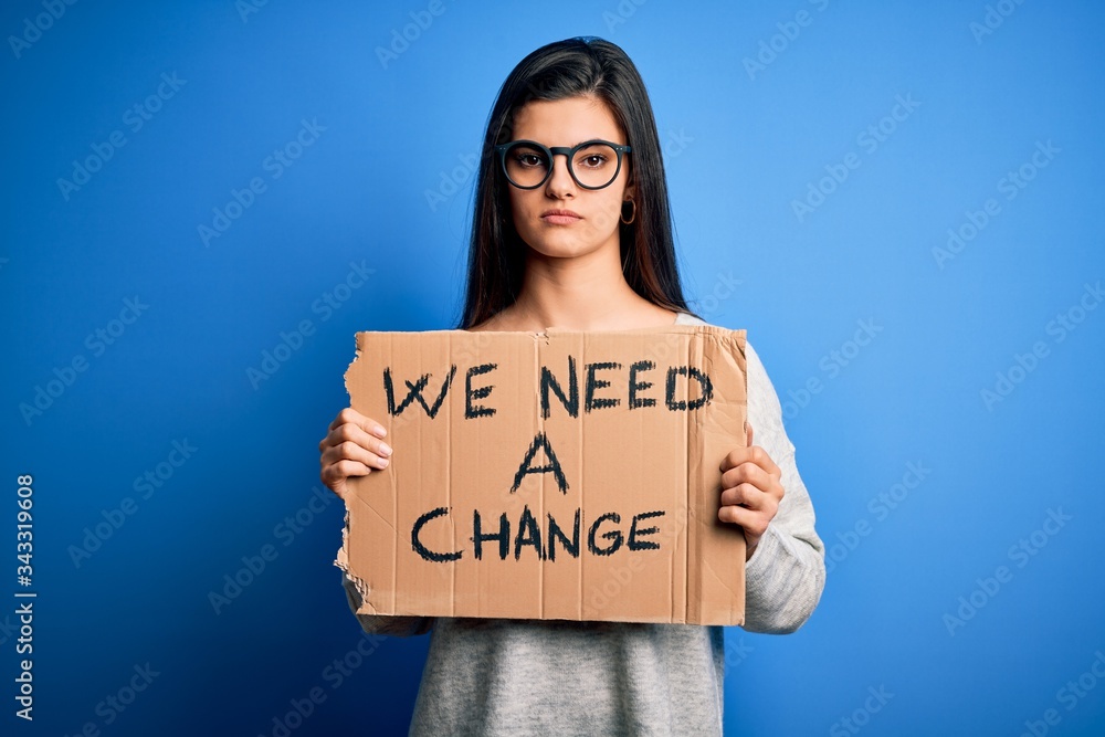 Young beautiful brunette activist woman holding banner protesting to change with a confident expression on smart face thinking serious Young beautiful brunette activist woman holding banner protesting to change with a confident expression on smart face thinking serious
