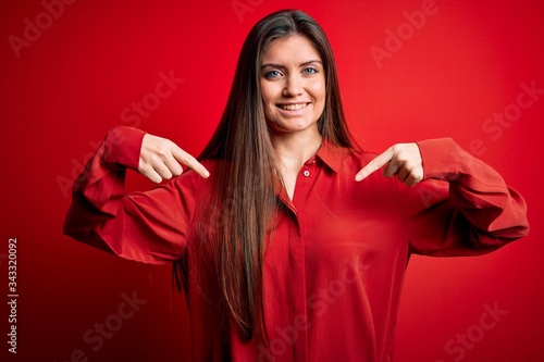 Young beautiful woman with blue eyes wearing casual shirt standing over red background looking confident with smile on face, pointing oneself with fingers proud and happy.