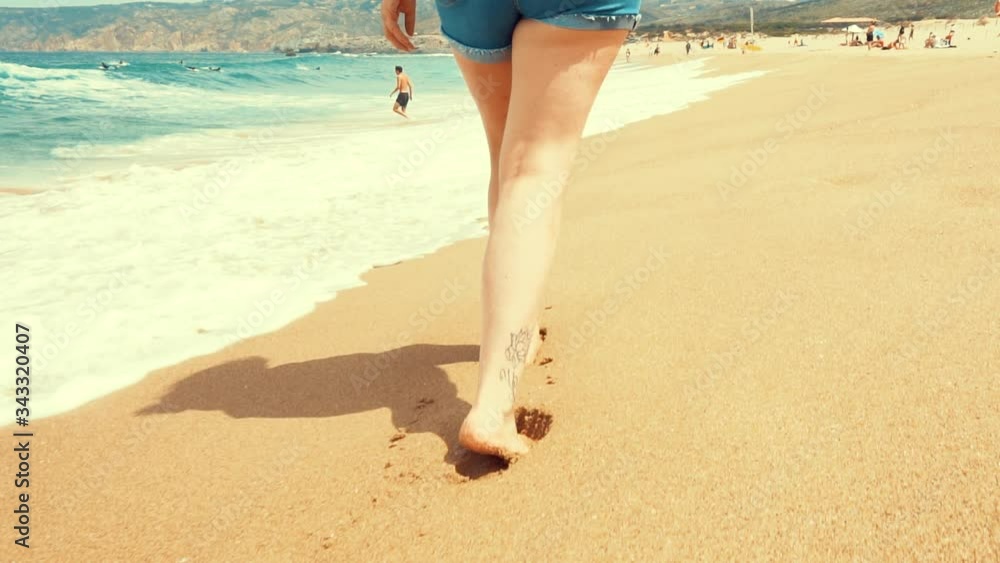 bonitos pies de chica paseando por la playa en la arena por la orilla del mar. cámara lenta