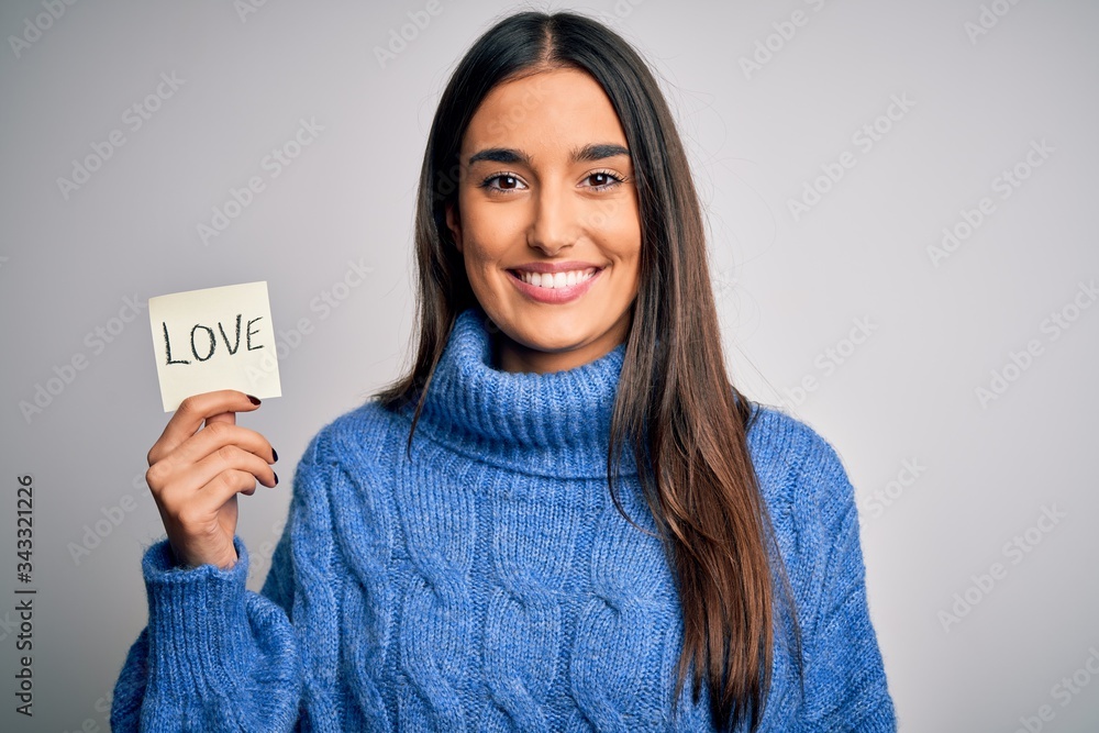 Young beautiful brunette romantic woman holding reminder paper with love message with a happy face standing and smiling with a confident smile showing teeth Young beautiful brunette romantic woman holding reminder paper with love message with a happy face standing and smiling with a confident smile showing teeth