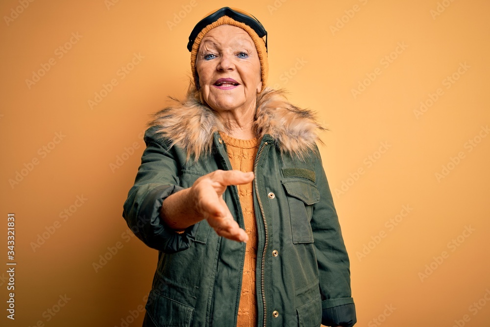 Senior beautiful grey-haired skier woman wearing snow sportswear and ski goggles smiling friendly offering handshake as greeting and welcoming. Successful business. Senior beautiful grey-haired skier woman wearing snow sportswear and ski goggles smiling friendly offering handshake as greeting and welcoming. Successful business.