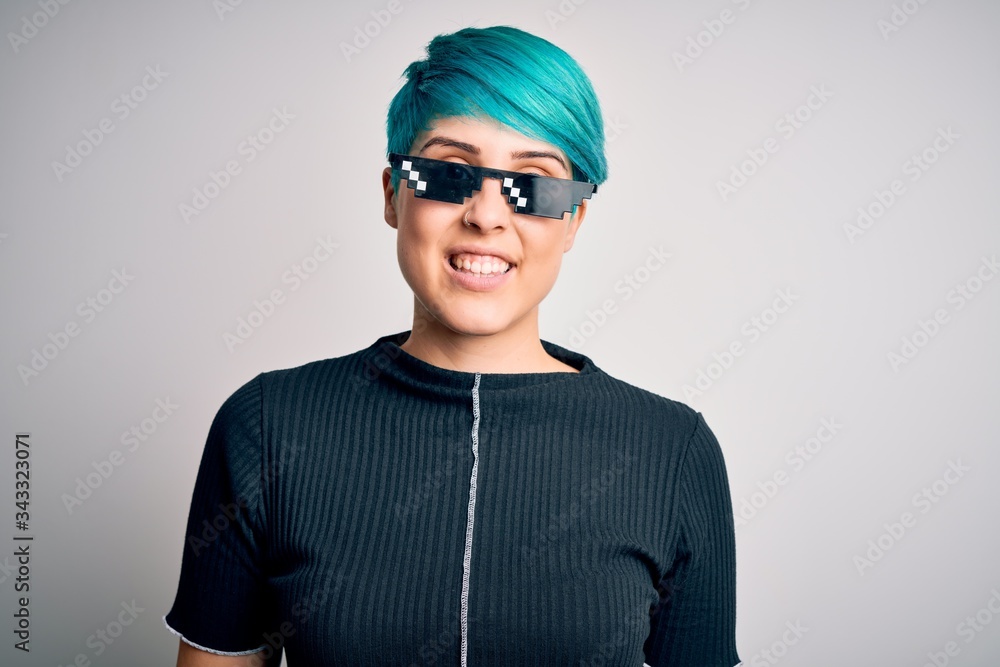 Young woman with blue fashion hair wearing thug life sunglasses over white background with a happy and cool smile on face. Lucky person. Young woman with blue fashion hair wearing thug life sunglasses over white background with a happy and cool smile on face. Lucky person.