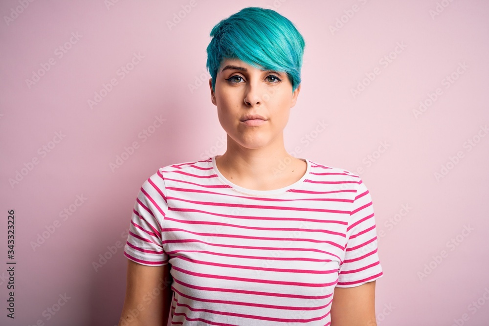 Young beautiful woman with blue fashion hair wearing casual striped t-shirt with serious expression on face. Simple and natural looking at the camera. Young beautiful woman with blue fashion hair wearing casual striped t-shirt with serious expression on face. Simple and natural looking at the camera.