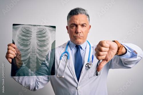 Middle age handsome grey-haired doctor man holding chest xray over white background with angry face  negative sign showing dislike with thumbs down  rejection concept