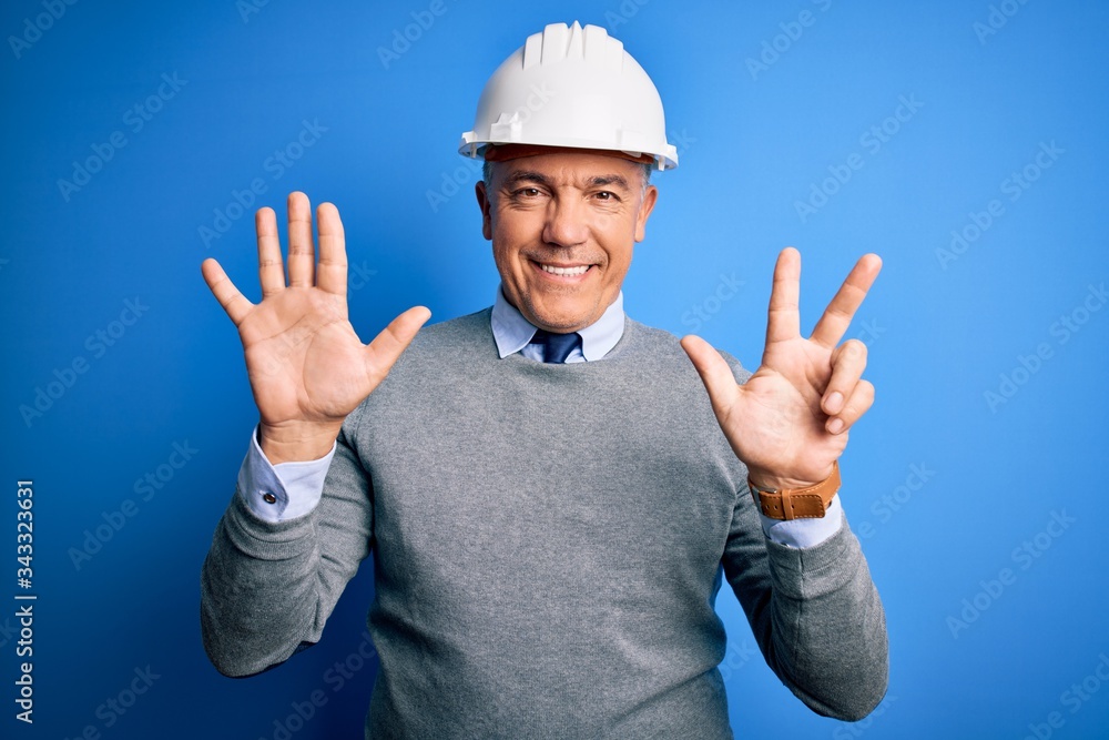 Middle age handsome grey-haired engineer man wearing safety helmet over blue background showing and pointing up with fingers number eight while smiling confident and happy.