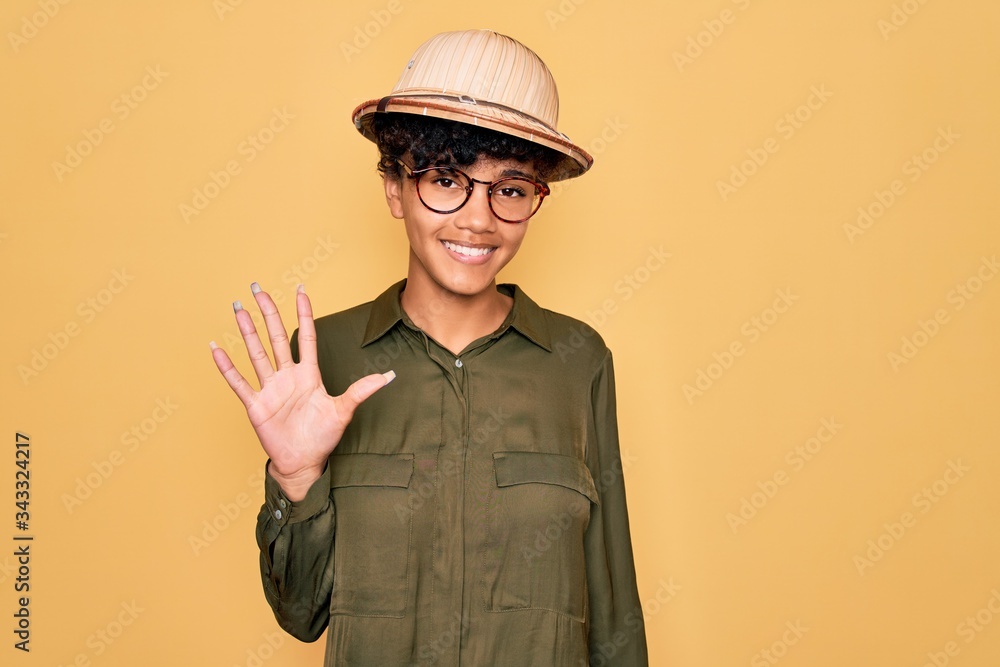 Young beautiful african american tourist woman wearing glasses and explorer hat showing and pointing up with fingers number five while smiling confident and happy. Young beautiful african american tourist woman wearing glasses and explorer hat showing and pointing up with fingers number five while smiling confident and happy.