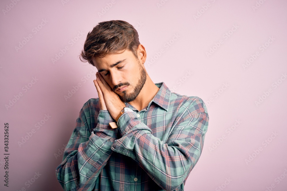 Young handsome man with beard wearing casual shirt standing over pink background sleeping tired dreaming and posing with hands together while smiling with closed eyes.