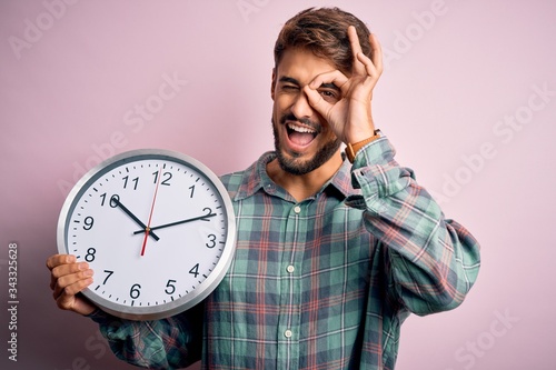 Foto Young man with beard doing countdown using big clock over isolated pink backgrou