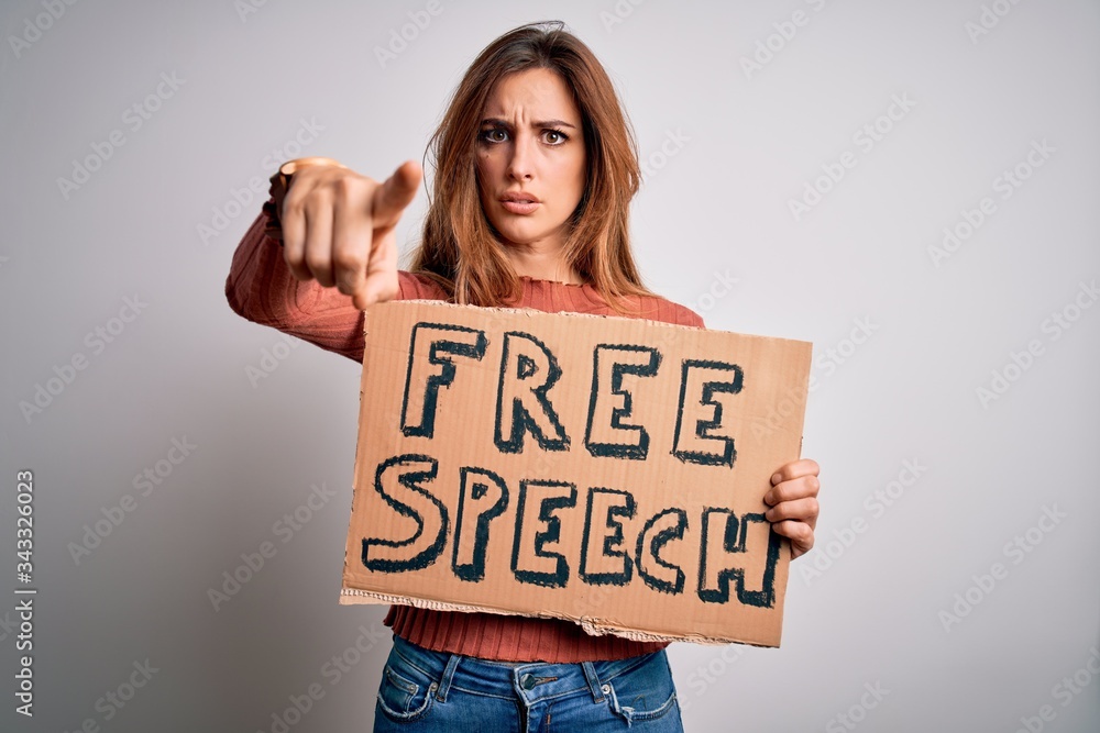 Young beautiful brunette woman asking for rights holding banner with free speech message pointing with finger to the camera and to you, hand sign, positive and confident gesture from the front Young beautiful brunette woman asking for rights holding banner with free speech message pointing with finger to the camera and to you, hand sign, positive and confident gesture from the front