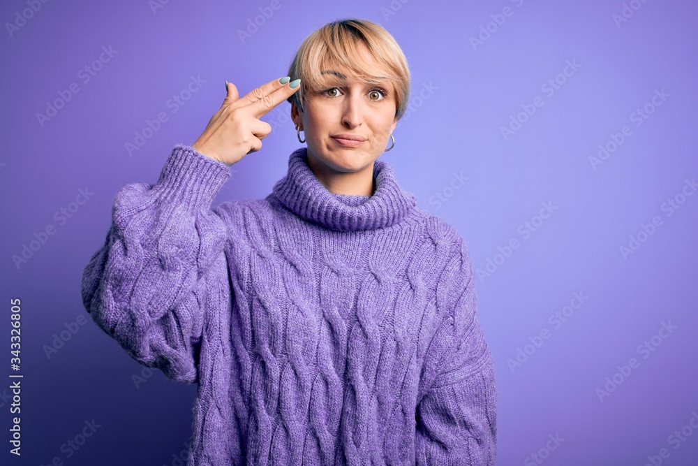 Young blonde woman with short hair wearing winter turtleneck sweater over purple background Shooting and killing oneself pointing hand and fingers to head like gun, suicide gesture. Young blonde woman with short hair wearing winter turtleneck sweater over purple background Shooting and killing oneself pointing hand and fingers to head like gun, suicide gesture.