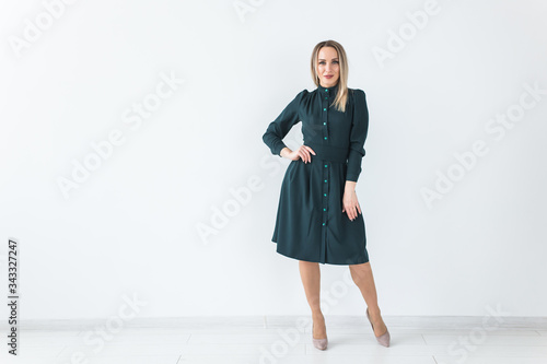 Fashionable young blonde woman in beautiful elegant dress posing at white studio with copy space.