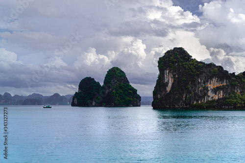 Daytime cloudy view of limestone pillars, calm water, and fisherman boat at Halong, Ha Long Bay, Vietnam