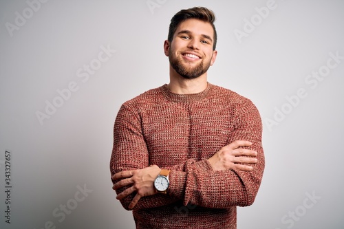 Young blond man with beard and blue eyes wearing casual sweater over white background happy face smiling with crossed arms looking at the camera. Positive person.