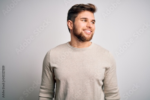 Young handsome blond man with beard and blue eyes wearing casual sweater looking away to side with smile on face, natural expression. Laughing confident. © Krakenimages.com