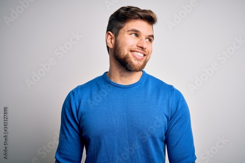 Young handsome blond man with beard and blue eyes wearing casual sweater looking away to side with smile on face, natural expression. Laughing confident. © Krakenimages.com