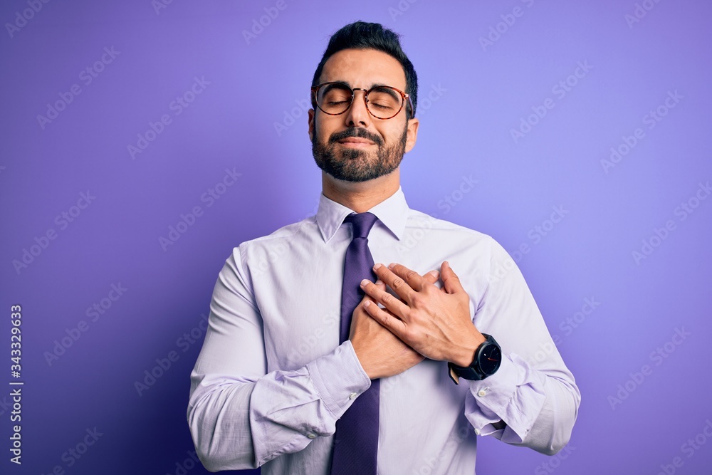 Handsome businessman with beard wearing casual tie and glasses over purple background smiling with hands on chest with closed eyes and grateful gesture on face. Health concept. Handsome businessman with beard wearing casual tie and glasses over purple background smiling with hands on chest with closed eyes and grateful gesture on face. Health concept.
