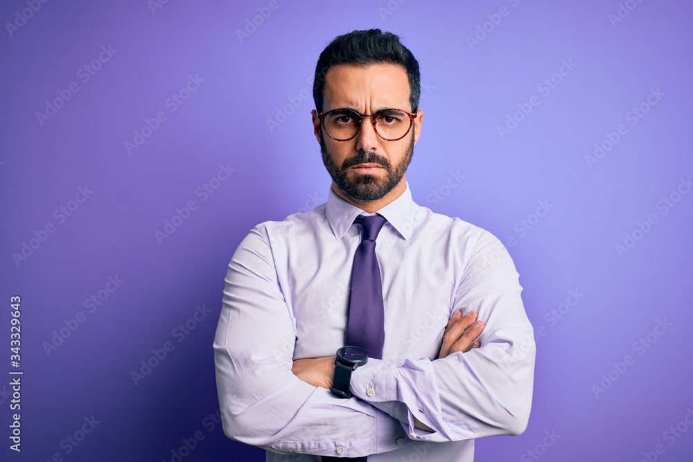 Handsome businessman with beard wearing casual tie and glasses over purple background skeptic and nervous, disapproving expression on face with crossed arms. Negative person. Handsome businessman with beard wearing casual tie and glasses over purple background skeptic and nervous, disapproving expression on face with crossed arms. Negative person.