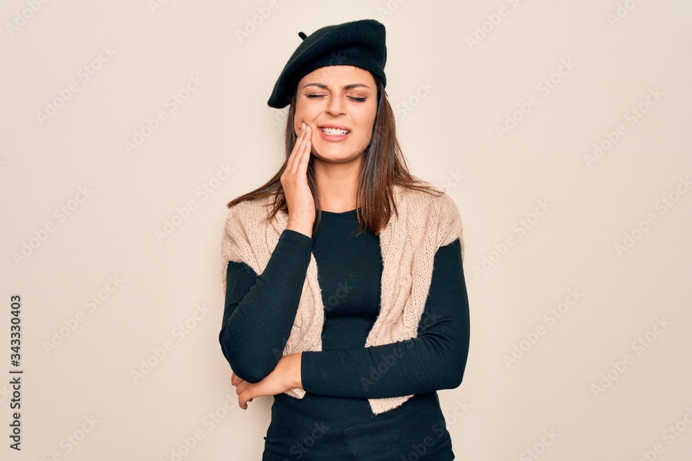 Young beautiful brunette woman wearing casual french beret over white background touching mouth with hand with painful expression because of toothache or dental illness on teeth. Dentist Young beautiful brunette woman wearing casual french beret over white background touching mouth with hand with painful expression because of toothache or dental illness on teeth. Dentist