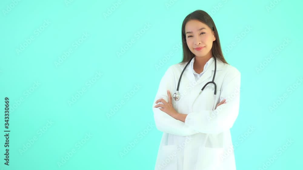 Static shot of a female Asian doctor standing in front of turquoise background wearing a coat and a stethoscope while smiling Static shot of a female Asian doctor standing in front of turquoise background wearing a coat and a stethoscope while smiling