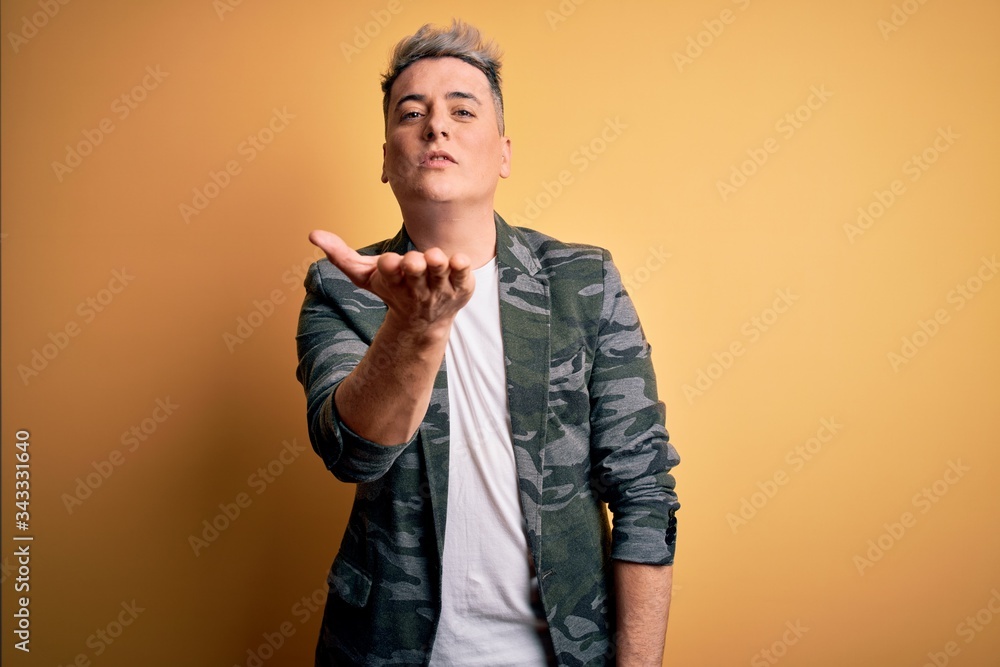 Young handsome modern man wearing business jacket standing over yellow isolated background looking at the camera blowing a kiss with hand on air being lovely and sexy. Love expression. Young handsome modern man wearing business jacket standing over yellow isolated background looking at the camera blowing a kiss with hand on air being lovely and sexy. Love expression.