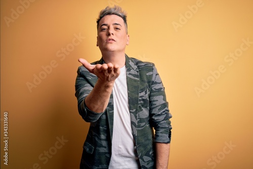 Young handsome modern man wearing business jacket standing over yellow isolated background looking at the camera blowing a kiss with hand on air being lovely and sexy. Love expression. © Krakenimages.com