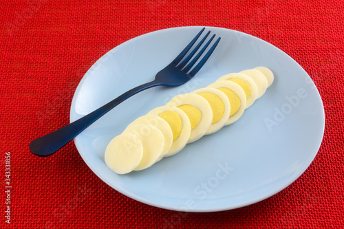 Hard boiled egg slices on blue breakfast plate with blue fork on red background