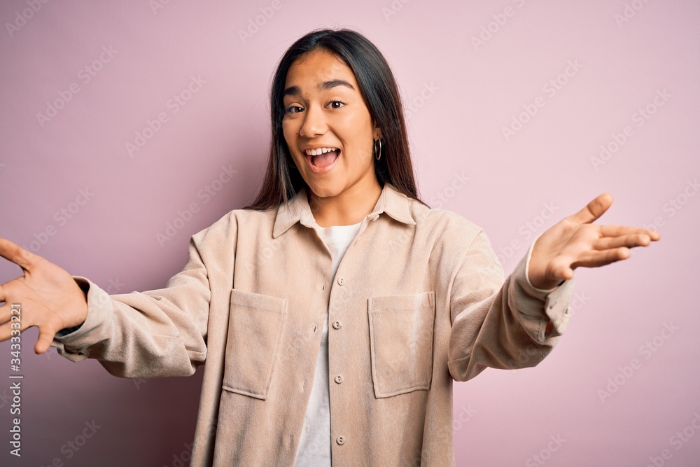 Young beautiful asian woman wearing casual shirt standing over pink background smiling cheerful offering hands giving assistance and acceptance. Young beautiful asian woman wearing casual shirt standing over pink background smiling cheerful offering hands giving assistance and acceptance.