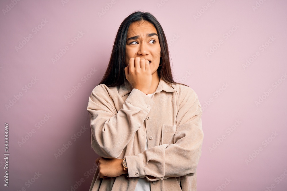 Young beautiful asian woman wearing casual shirt standing over pink background looking stressed and nervous with hands on mouth biting nails. Anxiety problem. Young beautiful asian woman wearing casual shirt standing over pink background looking stressed and nervous with hands on mouth biting nails. Anxiety problem.