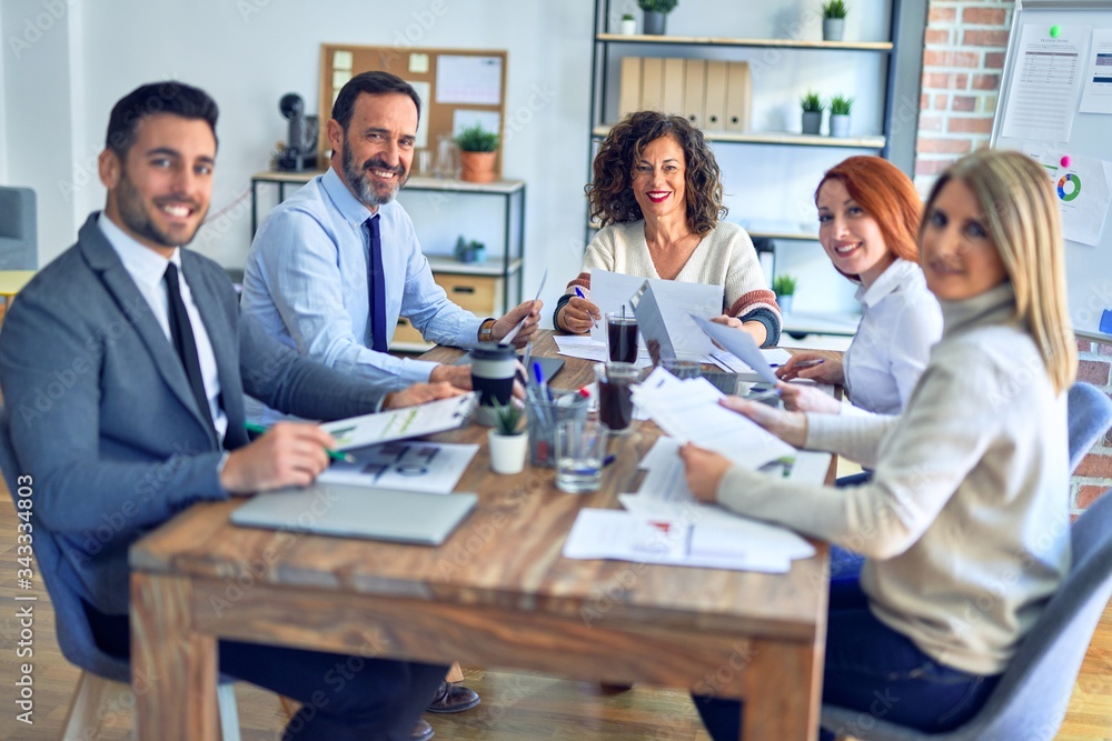 Fototapeta premium Group of business workers working together smiling happy. Sitting on desk posing with smile on face looking at the camera at the office