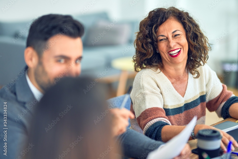 Group of business workers smiling happy working together. Sitting on desk speaking with smile on face at the office Group of business workers smiling happy working together. Sitting on desk speaking with smile on face at the office