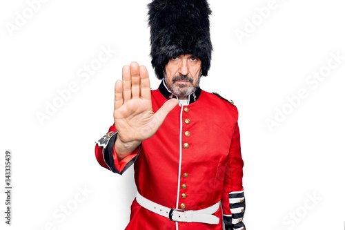 Middle age handsome wales guard man wearing traditional uniform over white background doing stop sing with palm of the hand. Warning expression with negative and serious gesture on the face.