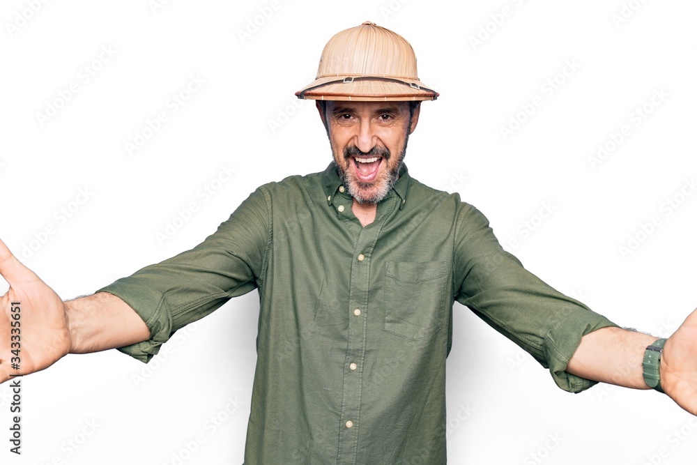 Middle age tourist man on vacation wearing explorer hat over isolated white background looking at the camera smiling with open arms for hug. Cheerful expression embracing happiness. Middle age tourist man on vacation wearing explorer hat over isolated white background looking at the camera smiling with open arms for hug. Cheerful expression embracing happiness.