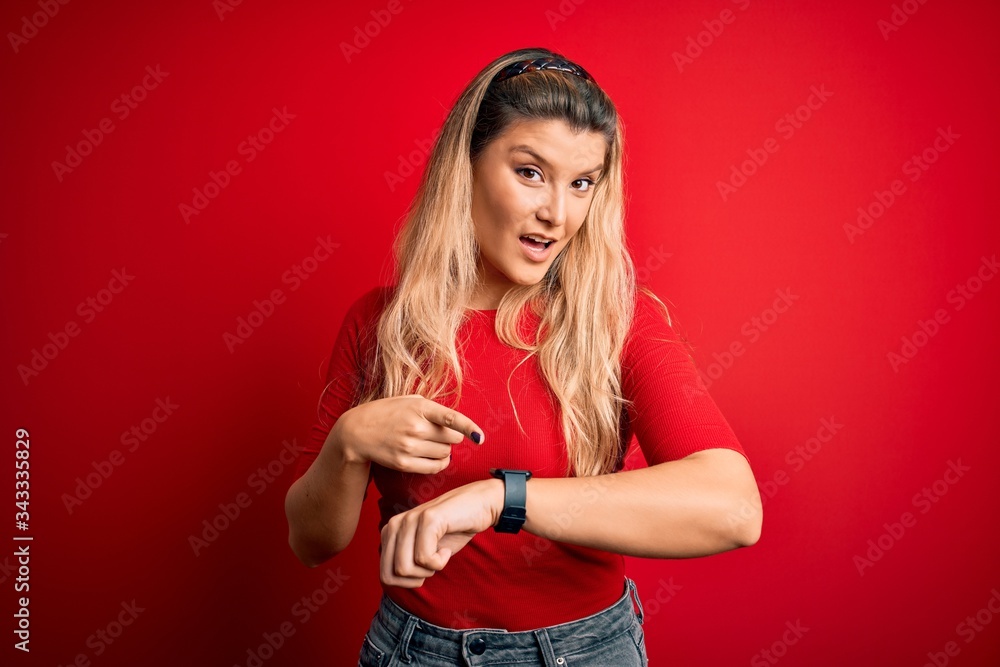 Young beautiful blonde woman wearing casual t-shirt standing over isolated red background In hurry pointing to watch time, impatience, upset and angry for deadline delay Young beautiful blonde woman wearing casual t-shirt standing over isolated red background In hurry pointing to watch time, impatience, upset and angry for deadline delay