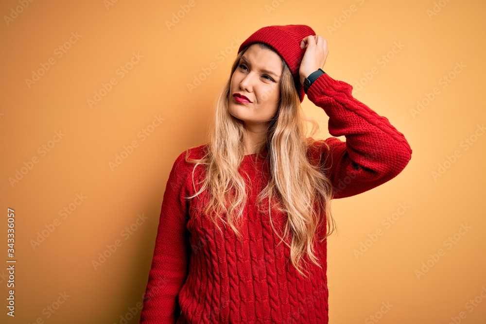 Young beautiful blonde woman wearing casual sweater and wool cap over white background confuse and wondering about question. Uncertain with doubt, thinking with hand on head. Pensive concept. Young beautiful blonde woman wearing casual sweater and wool cap over white background confuse and wondering about question. Uncertain with doubt, thinking with hand on head. Pensive concept.