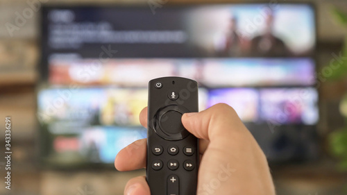 Male hand holding the TV remote control and changing TV channels
