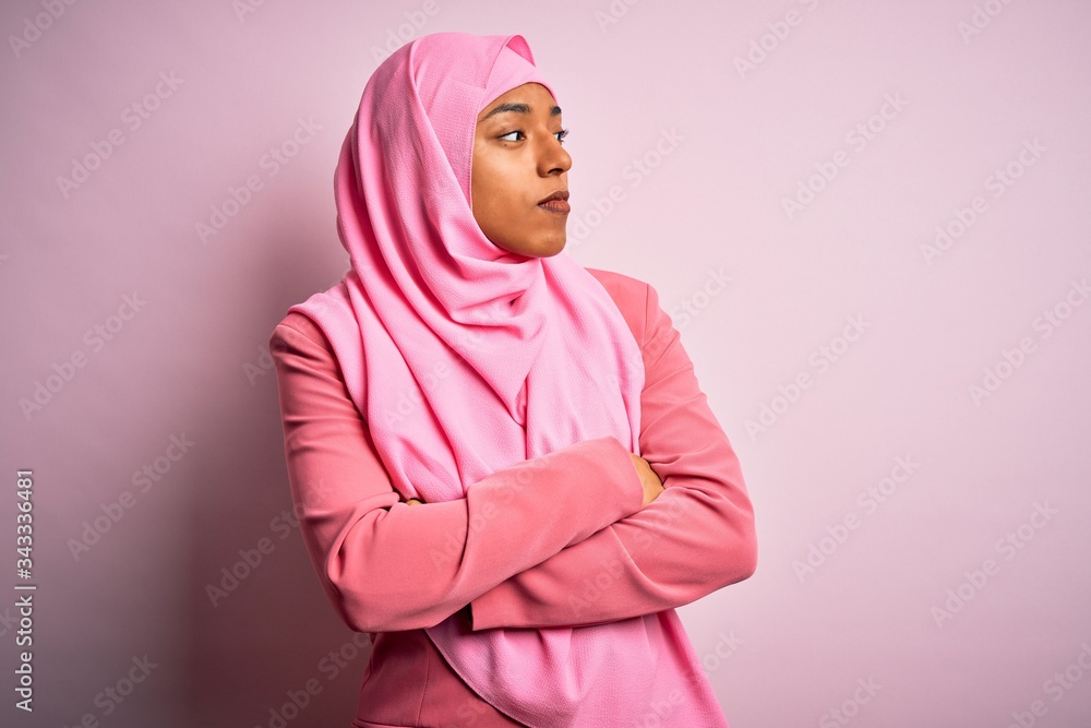 Fototapeta premium Young African American afro woman wearing muslim hijab over isolated pink background looking to the side with arms crossed convinced and confident